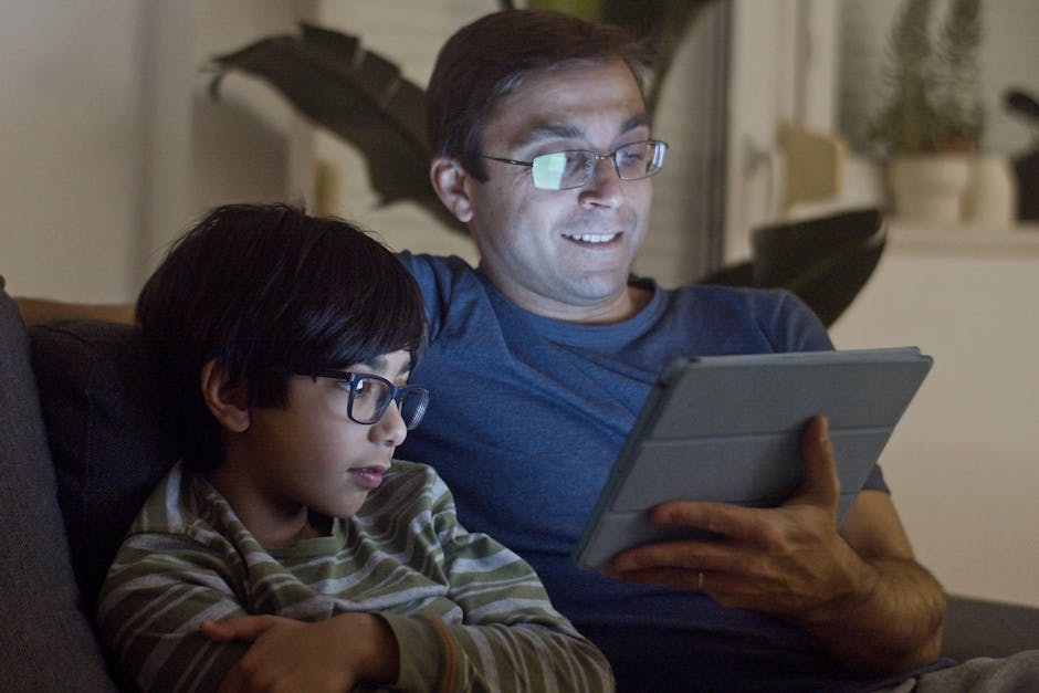 A father and son enjoy quality time using a tablet together indoors, creating a warm and intimate moment.